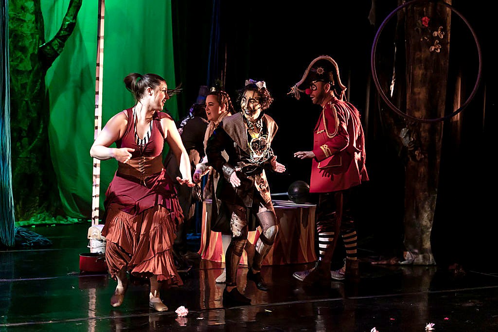 Ensemble cast performing on a green-lit forest stage set