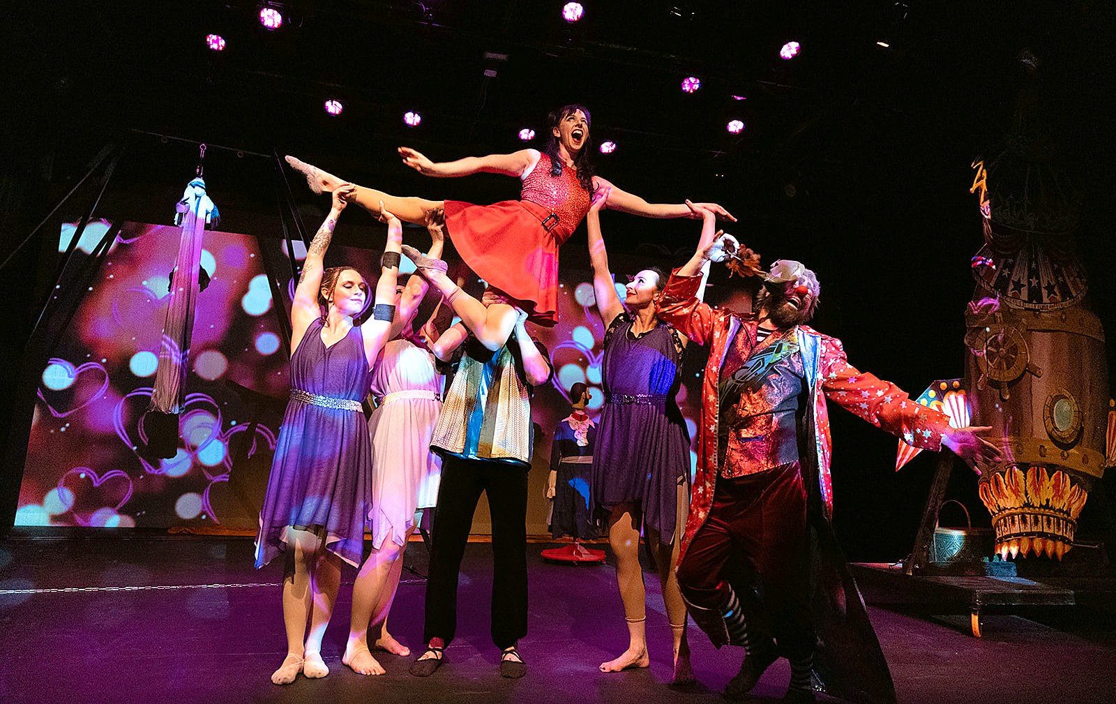Soul Penny Circus performers executing an aerial lift, clown character reaching up alongside them