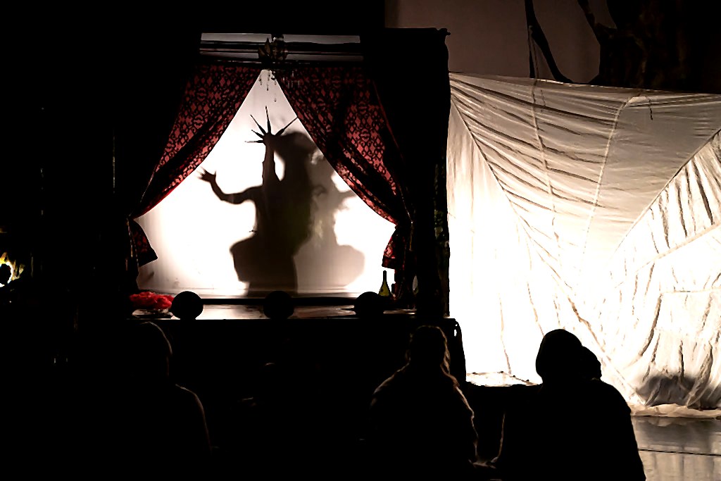 A shadow puppet performance behind a lit curtain, silhouetted figure with a starburst crown
